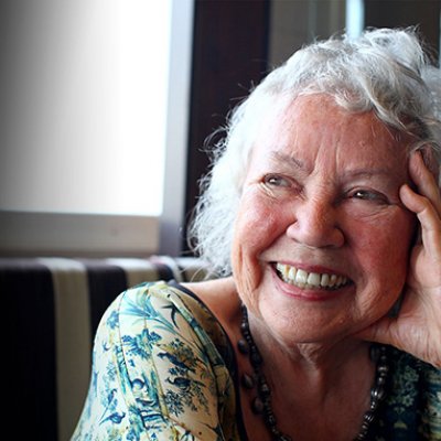 a grey-haired woman smiles resting her head on her hand